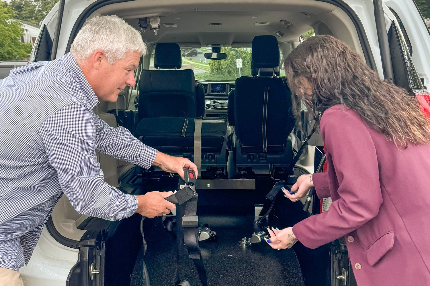 A man and a woman set up securement straps inside the back of an accessible minivan, preparing the interior for use.