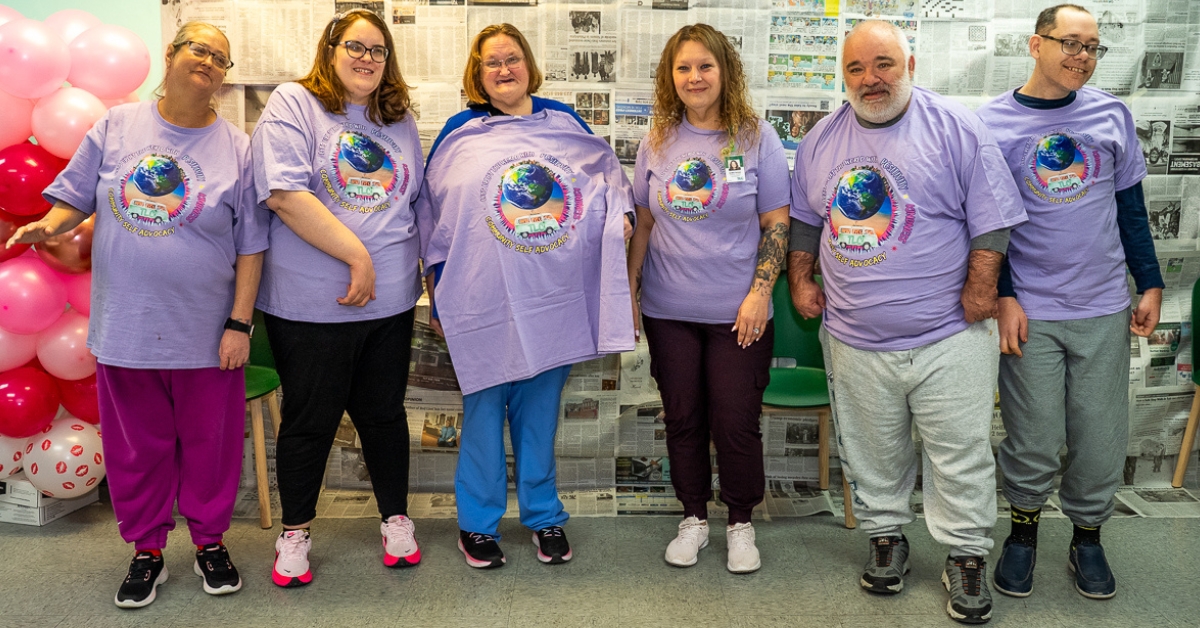 Members of TLC’s Community Self-Advocacy Committee stand together wearing matching purple shirts as they prepare to represent TLC at a community event.