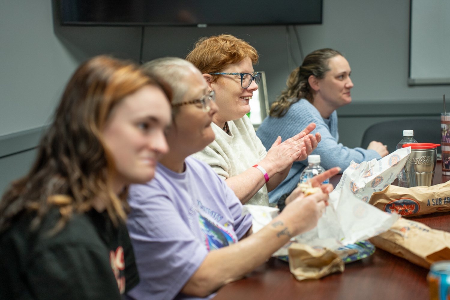 Members of TLC’s Community Self-Advocacy Committee sit together at a table during their monthly meeting, eating lunch and listening as one person speaks.