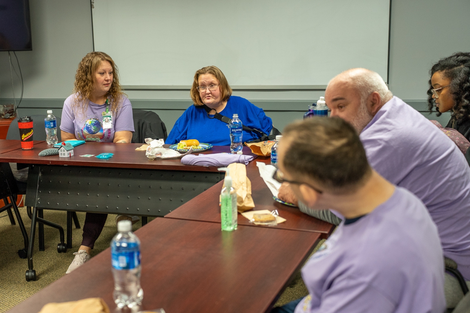 Members of TLC’s Community Self-Advocacy Committee gather around a table during their monthly meeting, sharing a meal and discussing plans together.